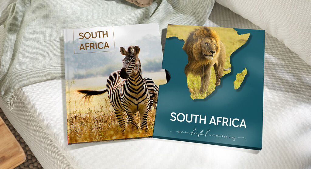 Two CEWE photo books with South Africa themes on a table. One shows a zebra, the other a lion and Africa's outline.