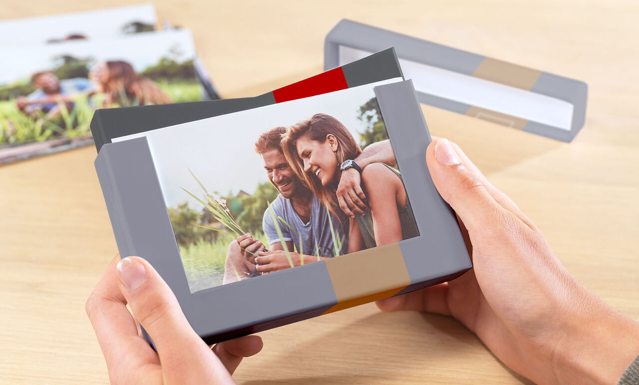 A person holds a photo book with a beautiful image in their hands. In the background are more photo books sharing emotional moments.