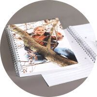 An open CEWE photo book on a table shows a charming picture of a child. A girl climbs a tree and smiles happily.