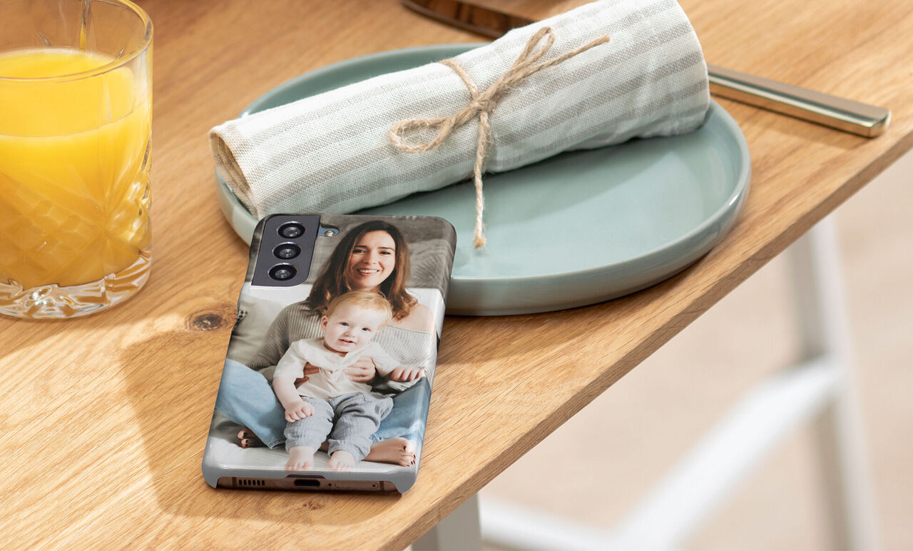 A smartphone with a loving photo design lies on a table next to a glass of orange juice and a set plate.