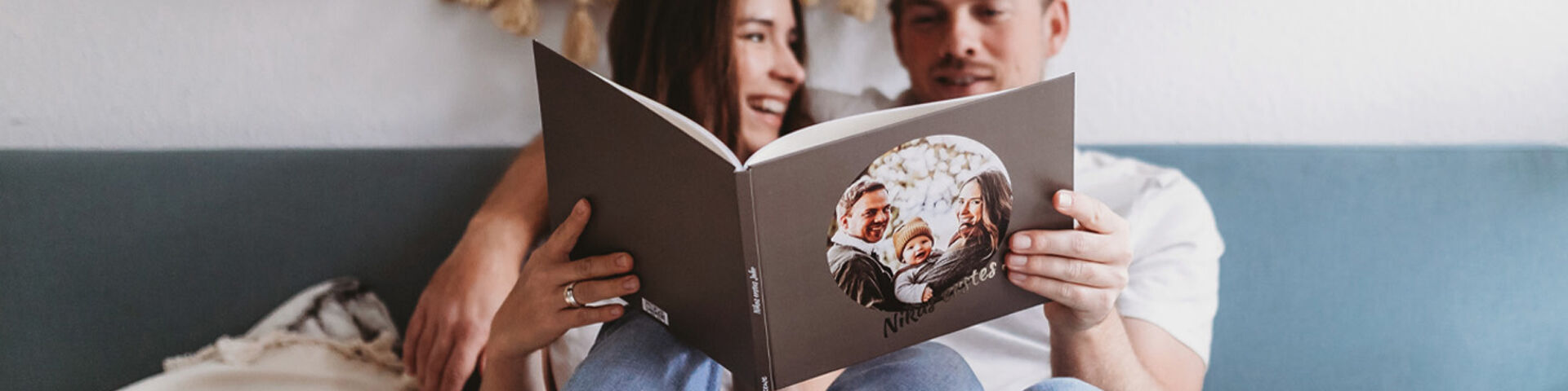 A happy couple reads a CEWE PHOTO BOOK on the sofa, enjoying shared memories