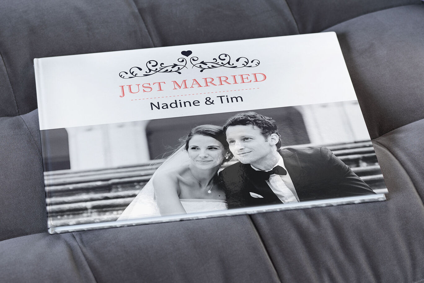 A CEWE PHOTO BOOK titled 'JUST MARRIED' on a gray couch.