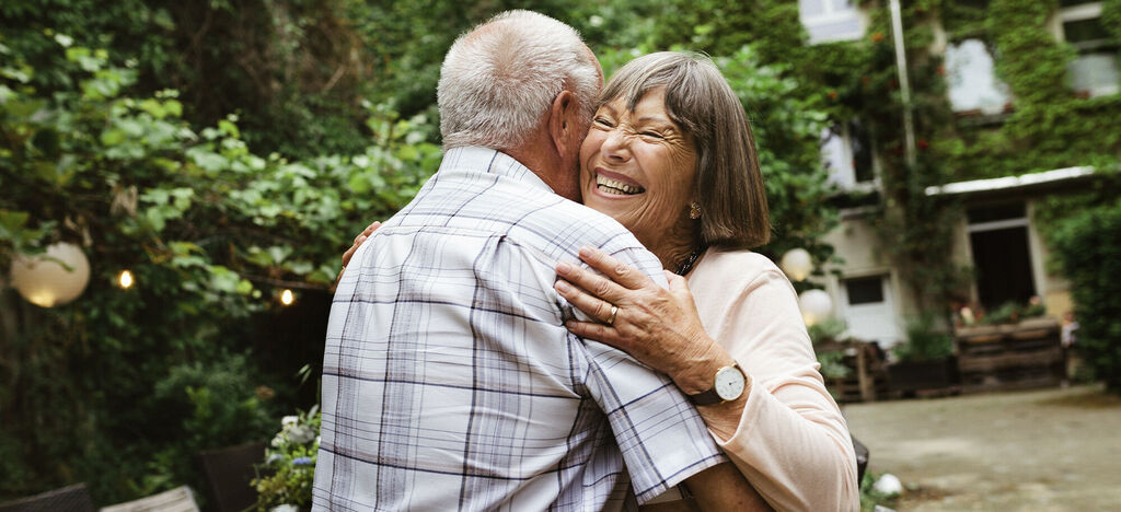 A happy elderly couple embracing in a garden full of green plants.