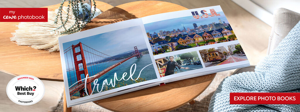 An open CEWE photo book with travel pictures on a table. It shows the Golden Gate Bridge and a city view.