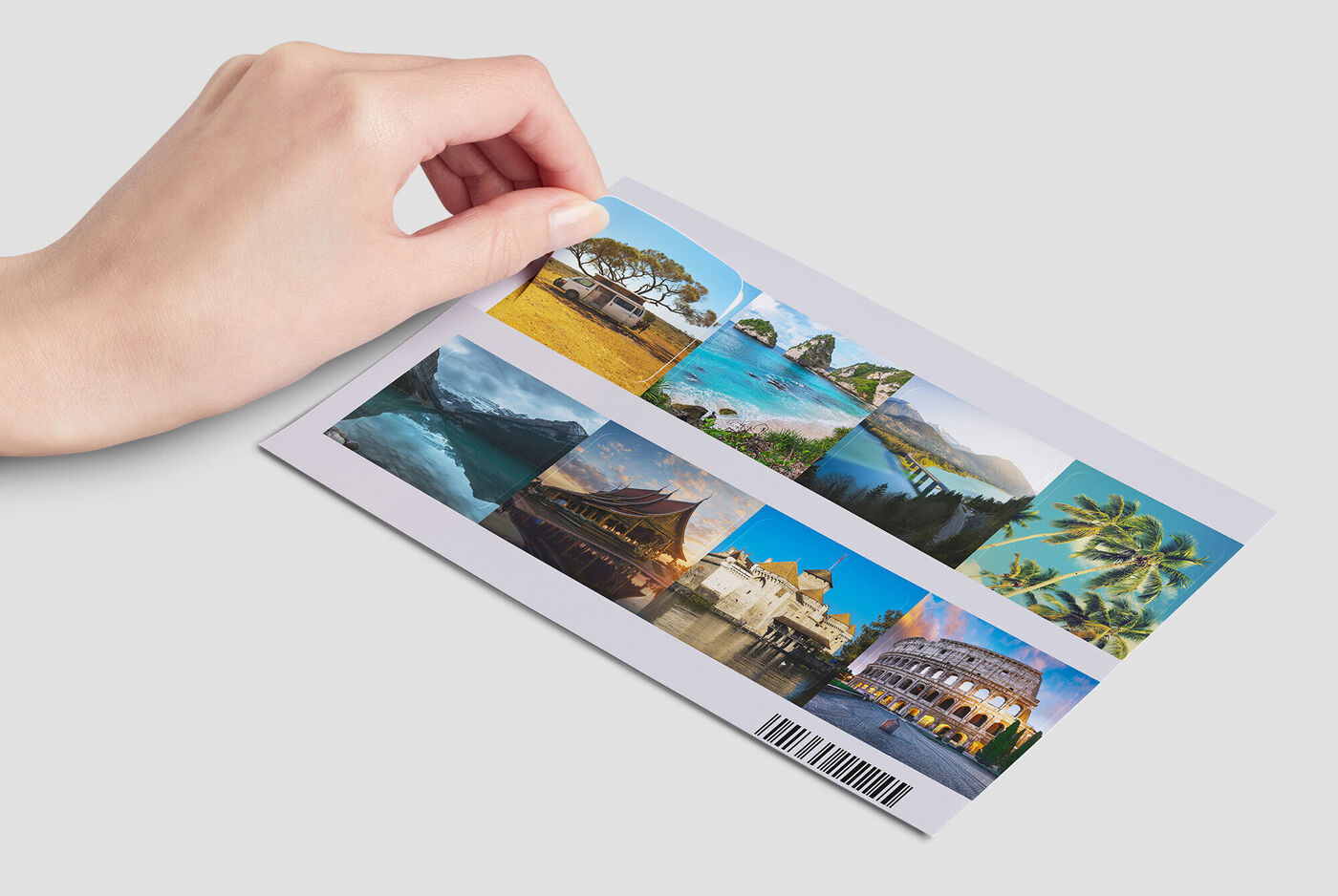 A hand holds a photo card with various vacation landscapes, including mountains, beach, and city.