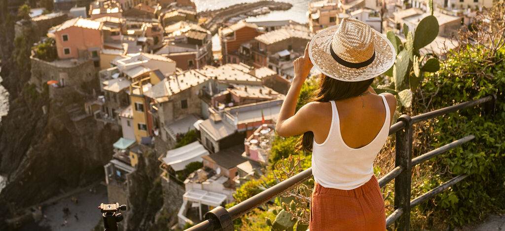 A woman with a straw hat gazes at the picturesque village by the sea.