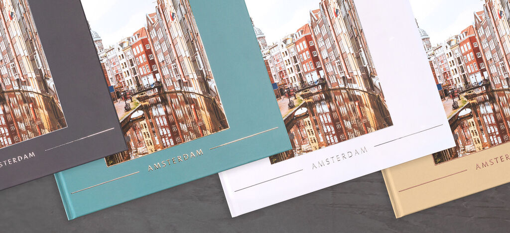 Three CEWE photobooks about Amsterdam in different colors are on a table.
