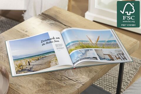 An opened Baltic Sea photo book on a table. The pages show beaches and coastal landscapes. CEWE PHOTO BOOK.