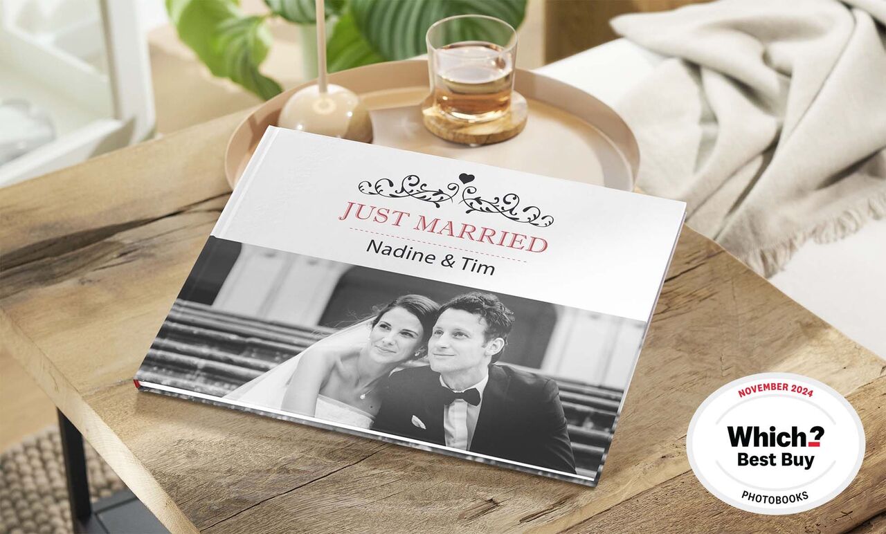A beautifully designed photo book titled 'Just Married' on a table, surrounded by a glass of water and a plant.