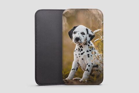 A cute Dalmatian puppy sits in a meadow with colorful flowers.