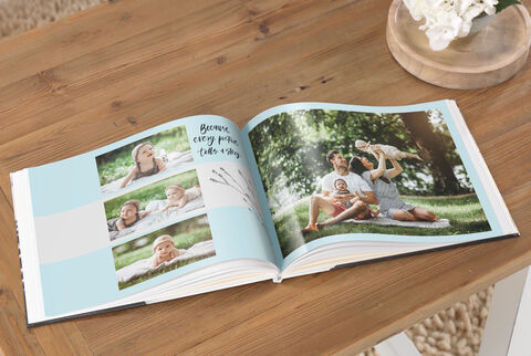 An open CEWE photo book with family photos on a table. It shows happy moments outdoors, surrounded by nature.