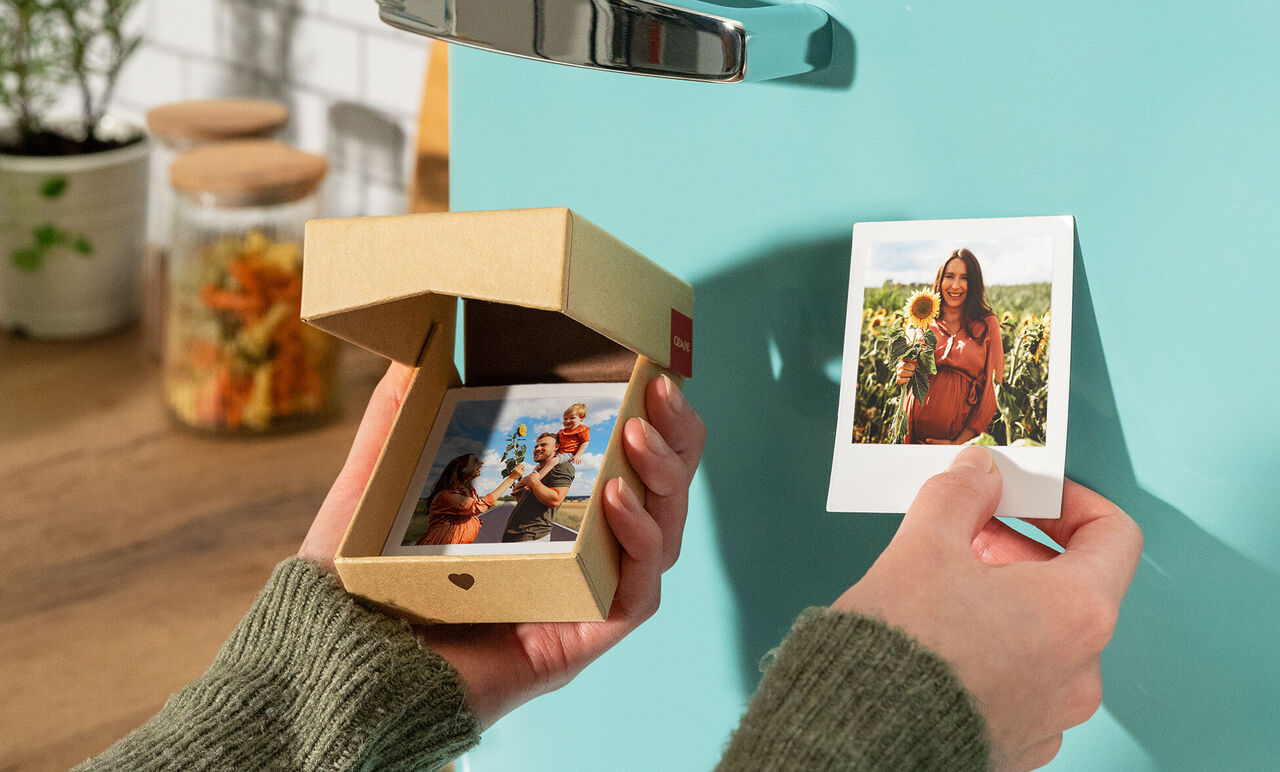 A person holds a small box with photos. A photo is hung on a green wall.