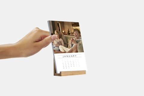 A person holding a CEWE photo calendar featuring a picture of two friends celebrating.