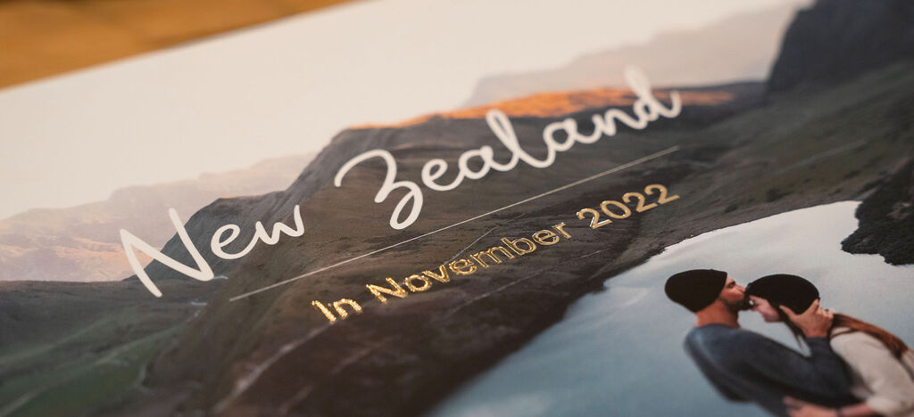A couple kisses in front of a picturesque alpine lake in New Zealand, with a headline 'New Zealand In November 2022' visible.
