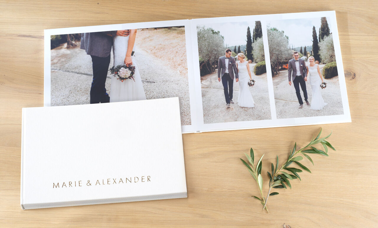 Wedding photo book titled "MARIE & ALEXANDER" on a table, next to a flower.