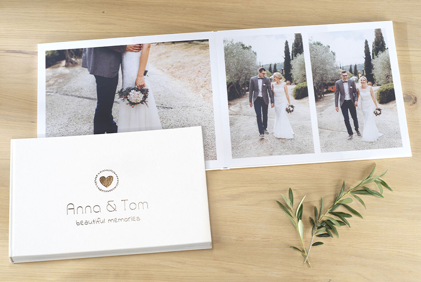 A CEWE photo book with a wedding couple walking along a path, surrounded by trees, and one open page showing two photos.
