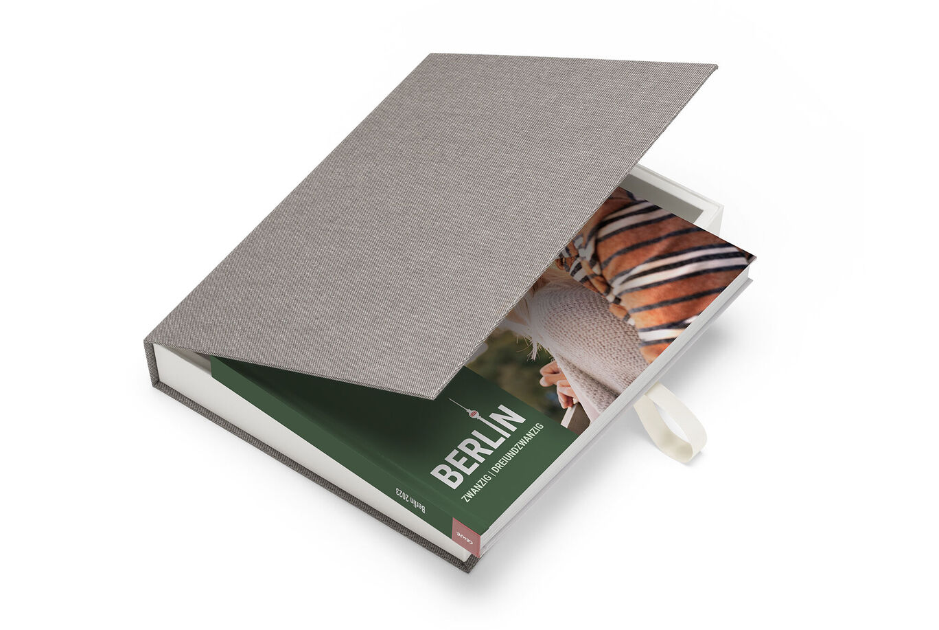 An open CEWE PHOTO BOOK with an image of Berlin inside and a gray fabric cover.