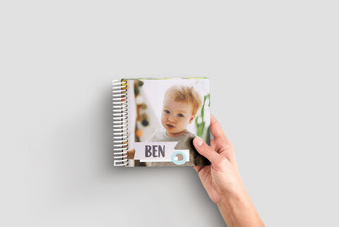 A person holds a lovingly designed photo book with a colorful cover in their hand.
