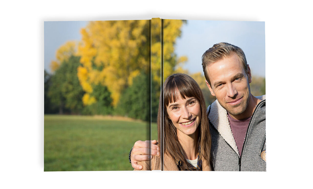 A couple holds a photo book in a green park surrounded by autumn trees