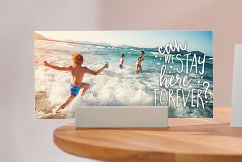 A boy happily jumps into the waves of the coast, while other kids play in the water. The text reads: 'Can we stay here forever?'