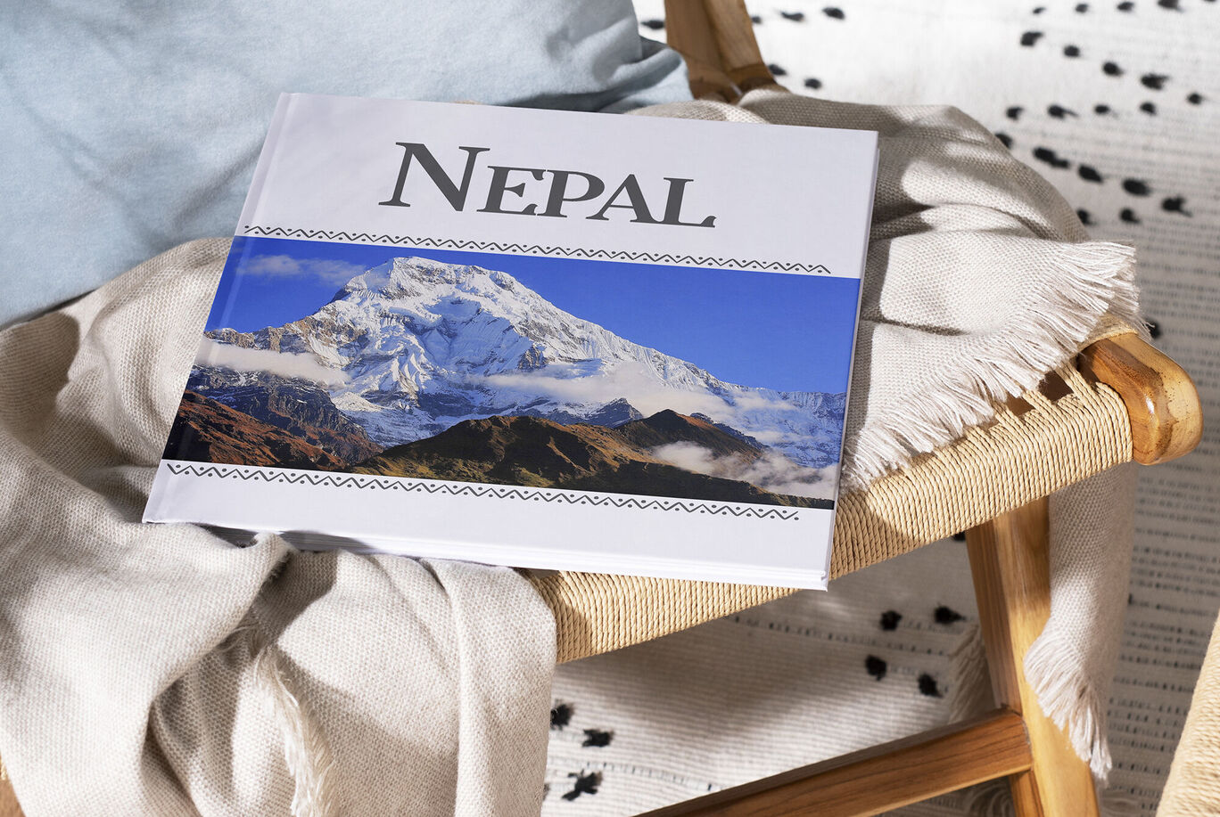 A CEWE photo book titled 'Nepal' lying on a chair. A mountain is visible in the background.