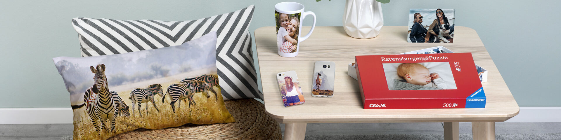 A cozy table with a CEWE PHOTO BOOK and various photo gifts, including a mug and a cushion with zebras.