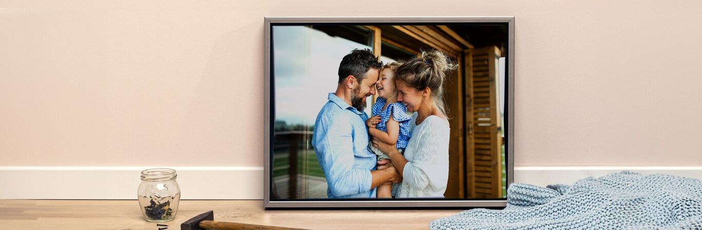 A happy family poses in front of a wooden house, the father holding his child.