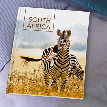 A CEWE photo book with a zebra on the cover standing in the African savanna.