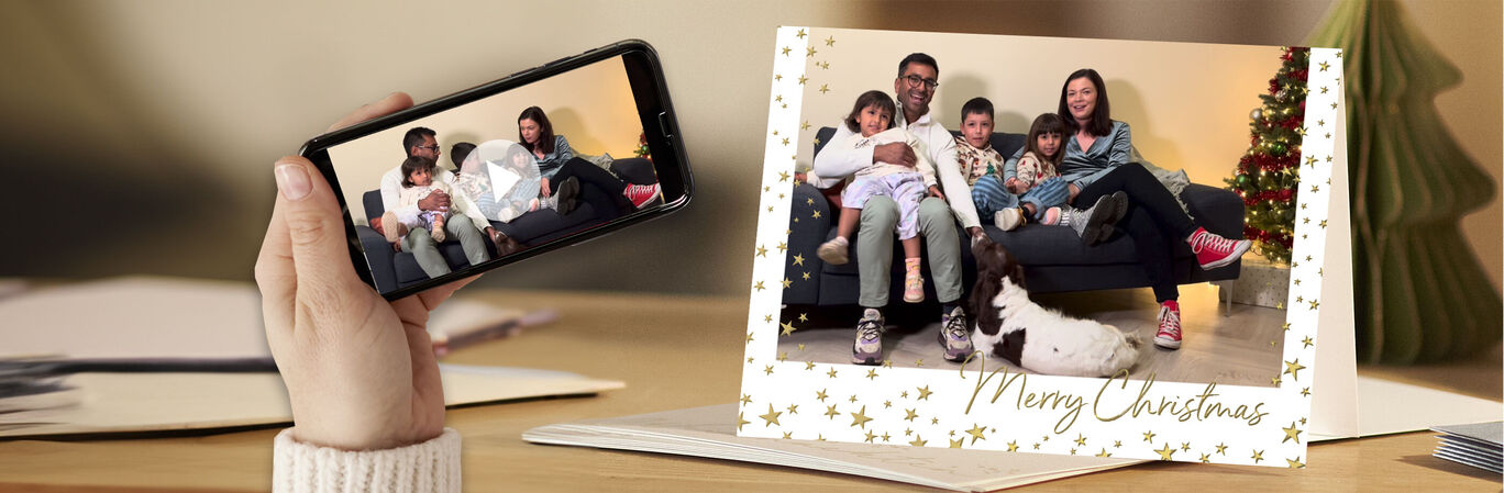 A family sits happily on a sofa holding Christmas cards. A beautiful Christmas tree stands in the background.