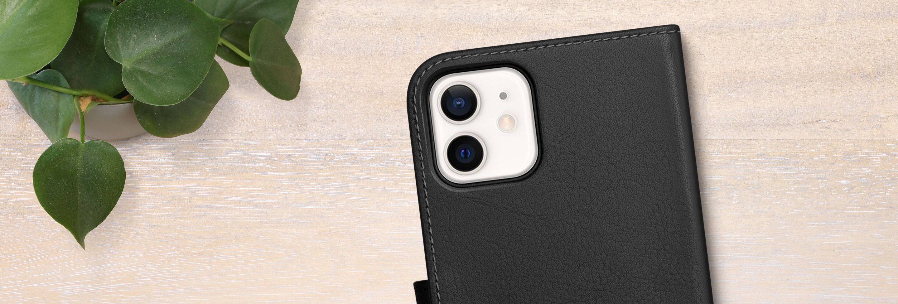 Black phone case with two camera lenses on a table with a plant in the background.