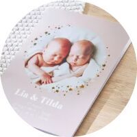 Two newborns, Lin and Tilda, lie in a gentle embrace on a soft background