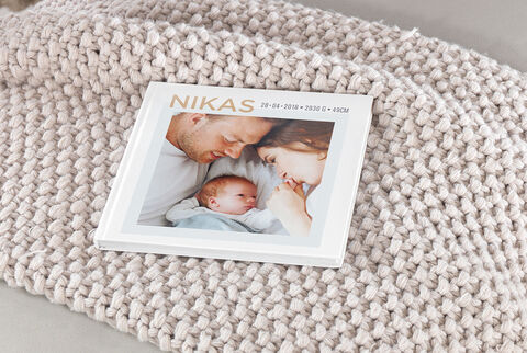 A lovingly designed CEWE photo book lies on a warm blanket. The cover shows names and the date of a special moment.
