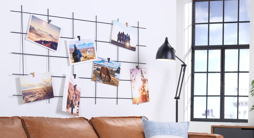 Photos hanging on a grid wall next to a couch and a lamp.