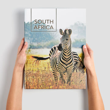 A person holds a photo book with a zebra on the cover in their hand.