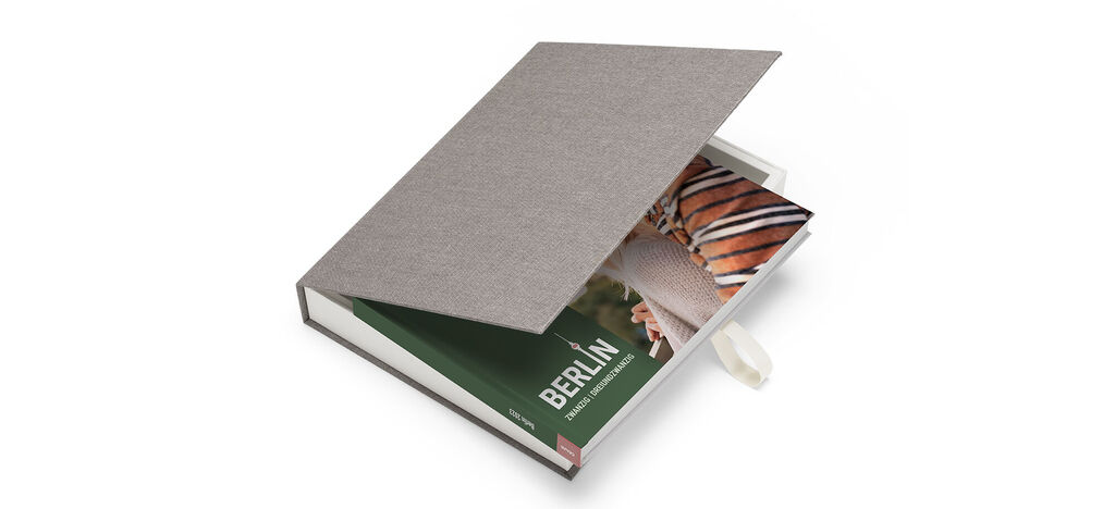 A CEWE PHOTOBOOK lays open with a welcoming green page and a photo of Berlin