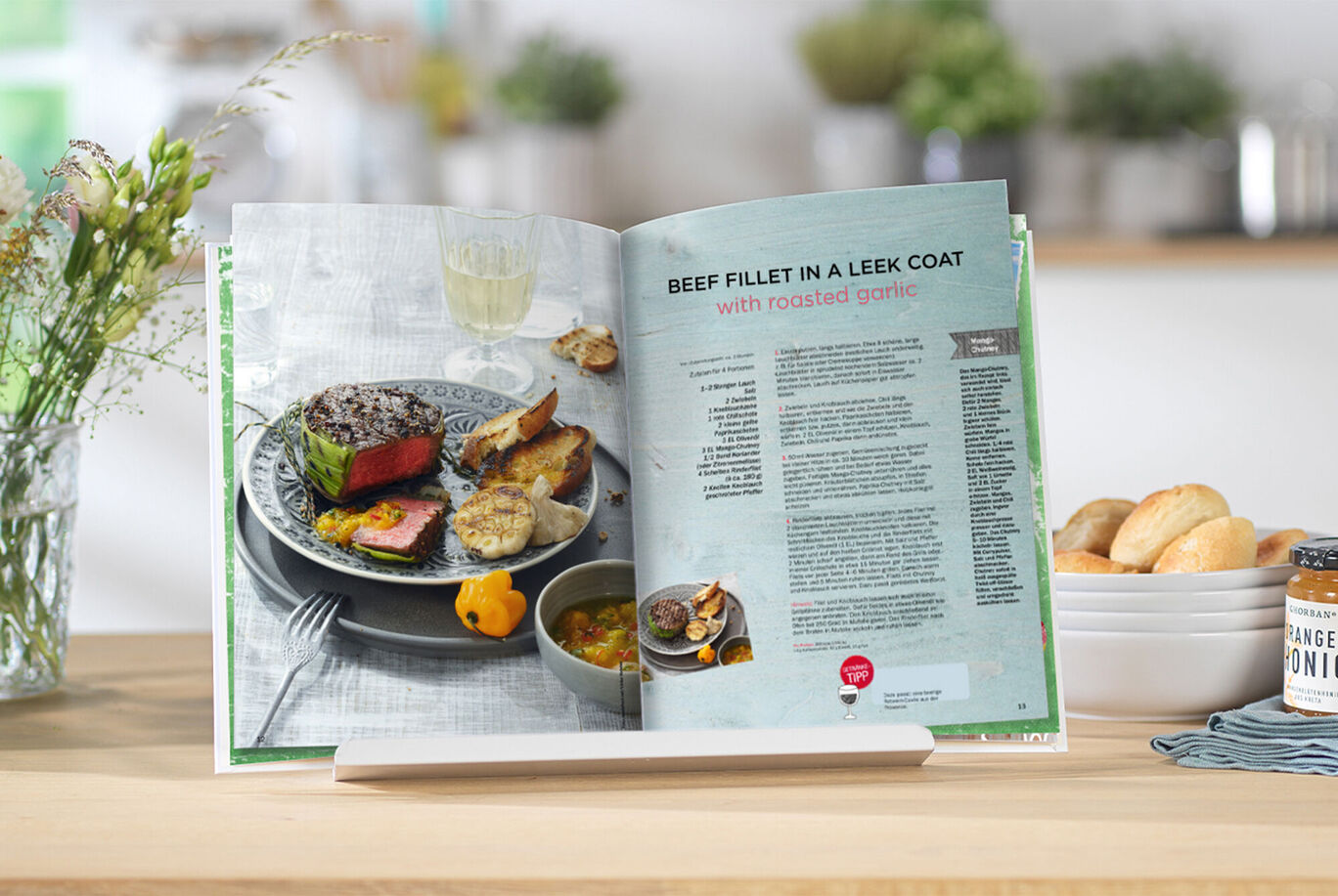 Open cookbook with a recipe for beef fillet in leek wrap, alongside side dishes on a table.