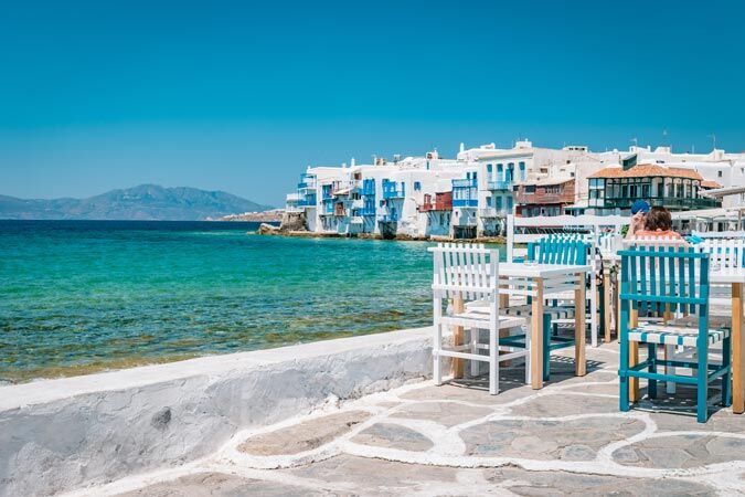Blue and white chairs by the water in front of a place with white buildings.