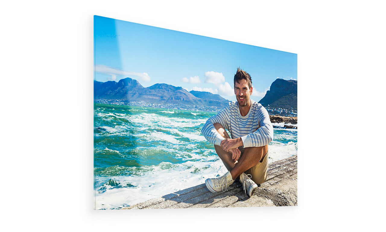 A man sits on the beach with a view of the sea and mountains in the background
