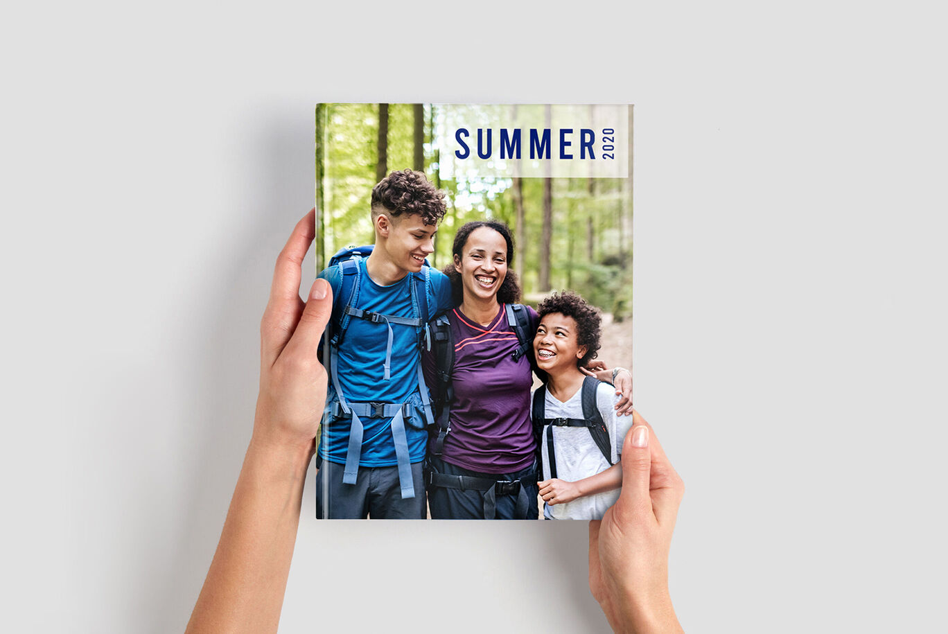A person holding a photo book titled "SUMMER 2020" in a forest setting.