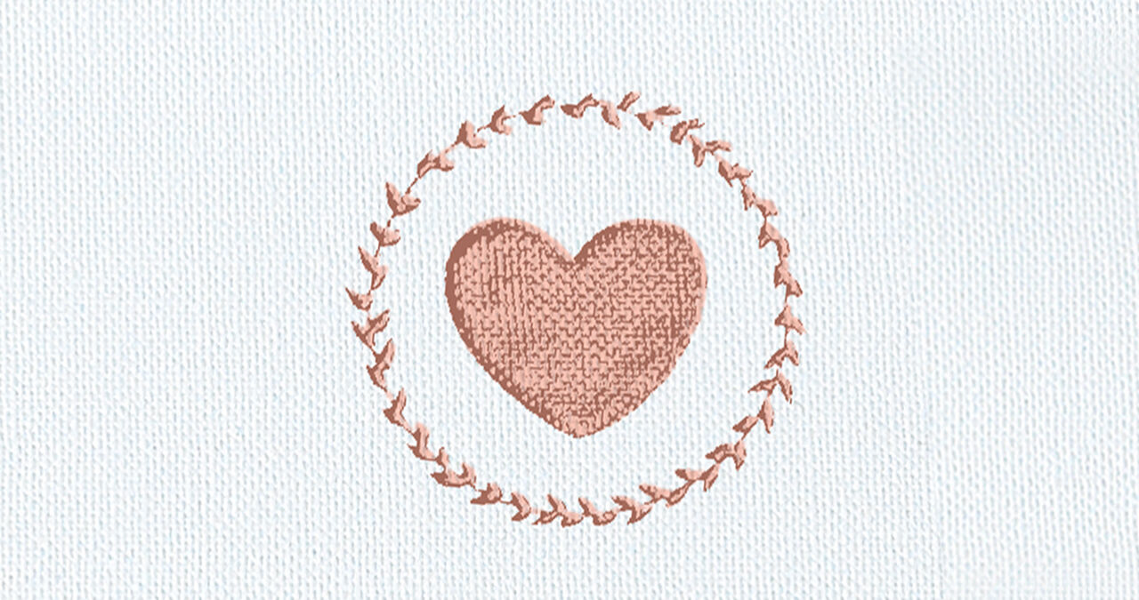 Delicately embroidered heart in a wreath of small, fine stitches on light fabric.