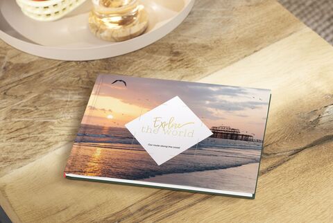 CEWE PHOTO BOOK 'Explore the World' with a sunset image on the cover, on a wooden table.
