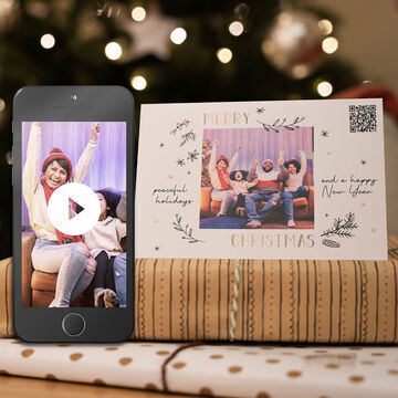 A smartphone shows a cheerful Christmas video. Next to it is a festive card with 'Merry Christmas' and a QR code.