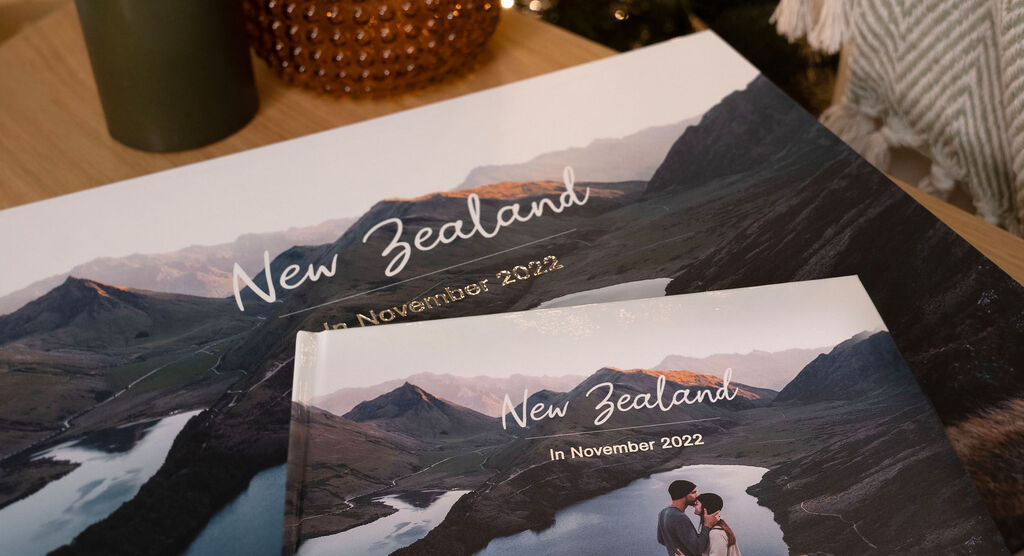 Two photo books featuring landscapes from New Zealand, one large and one small, on a table.
