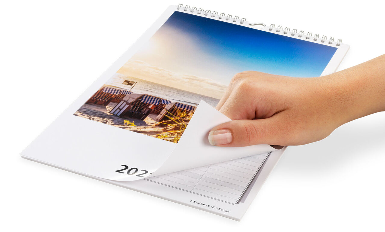 A hand flips through a CEWE photo calendar with a beautiful beach motif.