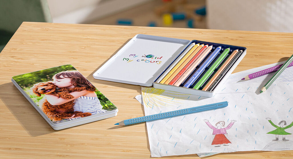 A girl hugs her dog on a photo book, next to a box of colored pencils and drawings.