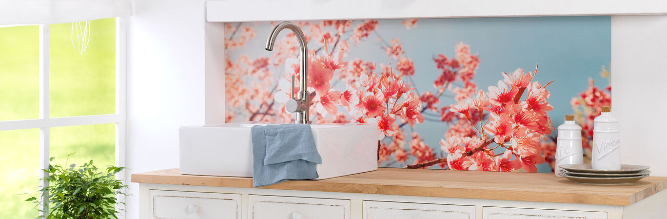A modern kitchen design with a white sink, a blue towel, and blooming cherry blossom wall decoration in the background