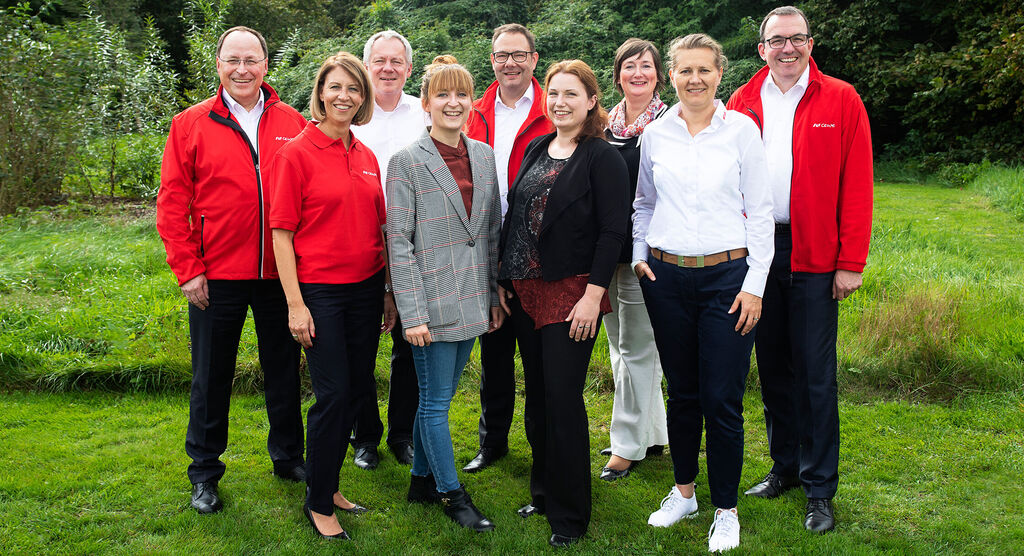A group of people smiling in nature, wearing matching red tops representing team spirit and joy.
