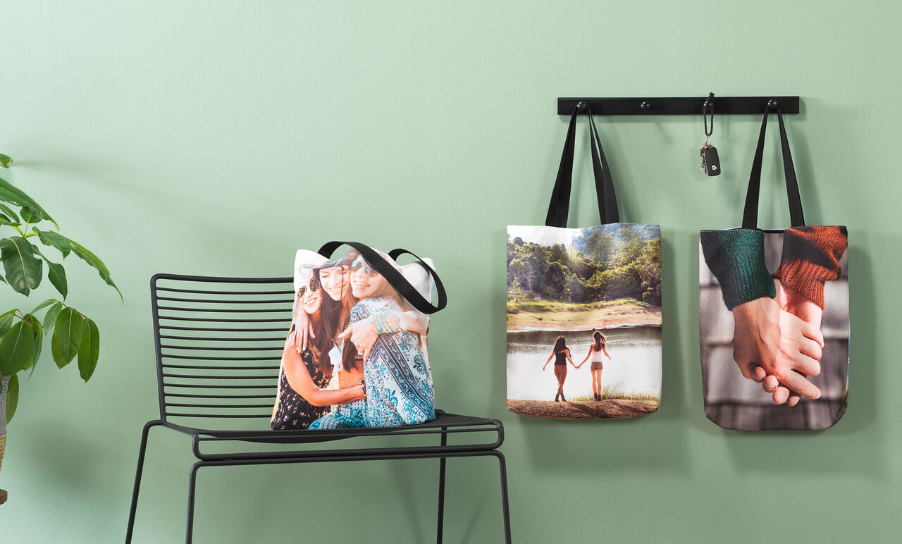 Three creative bags with personal photo motifs hang on a wall shelf. One shows two friends, another a dreamy landscape, and the third pairs holding hands.