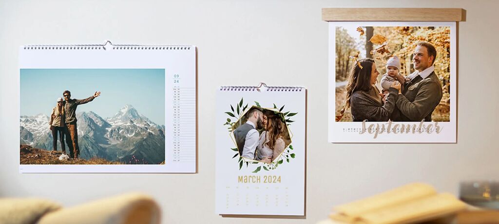 Three varied photo calendars on a wall: one with a mountain photo, one with a couple photo, and a monthly theme.