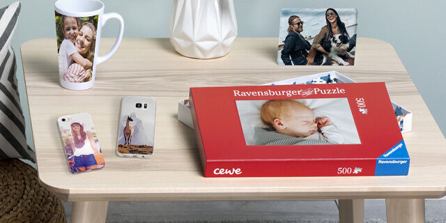 A table with a Ravensburger puzzle, a mug with personal photos, mobile phones with photo covers, and a picture frame with memories.
